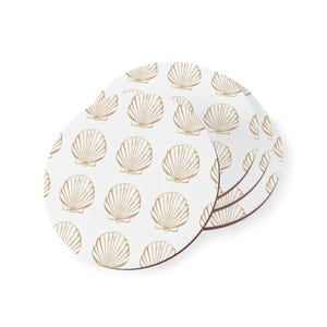 May include: A set of circular coasters featuring a repeating pattern of tan-coloured scallop shells printed on a white background. Each coaster has a smooth, round edge and a consistent design showing multiple shell illustrations in a uniform layout.