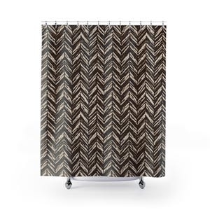 May include: A shower curtain with a repeating chevron pattern in shades of brown and beige. The design features a series of angled lines, creating a textured, artistic look. The curtain hangs from a metal rod with chrome-colored rings.