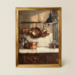 Op de afbeelding: Een ingelijst schilderij van een keuken met koperen potten die aan een rek boven een houten kast hangen. De potten zijn in een rij gerangschikt, met de grootste pot in het midden. De kast heeft twee laden en een deur. Het schilderij is geplaatst tegen een lichtbruine achtergrond.