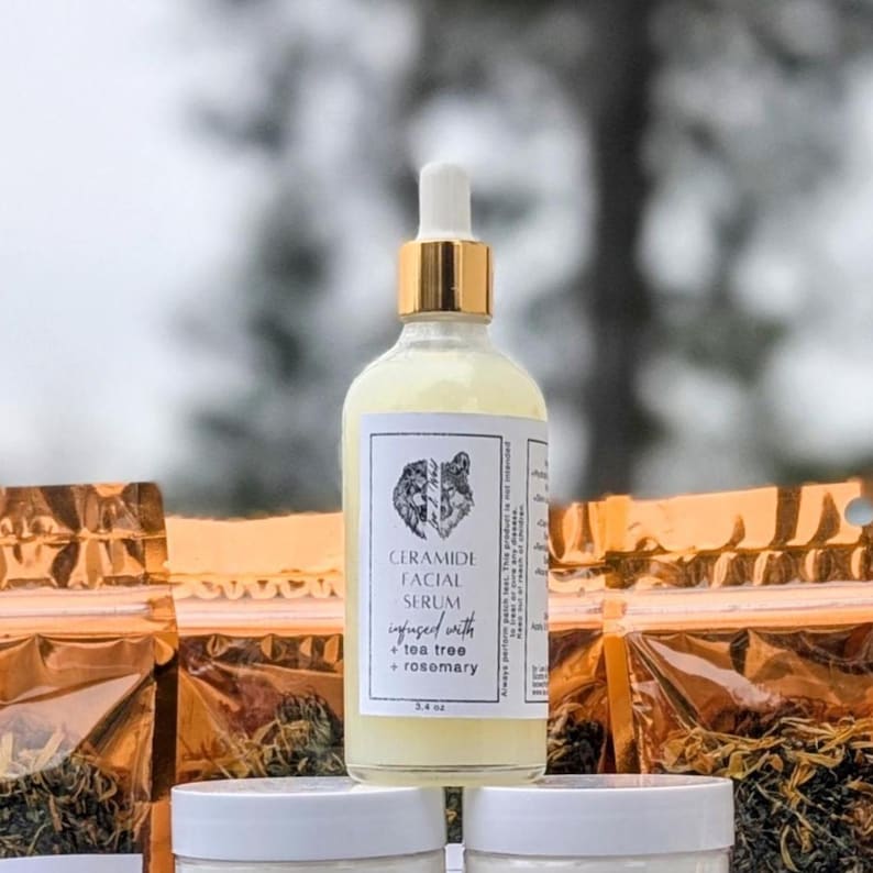 May include: A clear glass bottle of Ceramide Facial Serum with a gold dropper top. The label features a wolf design and text indicating it's infused with tea tree and rosemary. The bottle is 3.4 fl oz. Other products are in the background.