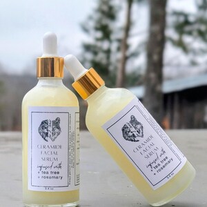 May include: Two bottles of Ceramide Facial Serum, infused with tea tree and rosemary, are displayed. The bottles have white labels with a wolf illustration and gold-colored droppers. Each bottle contains 3.4 oz of serum.