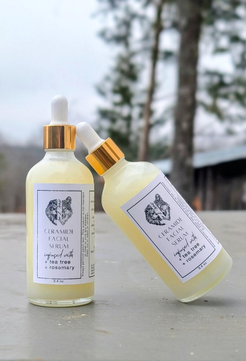 May include: Two bottles of Ceramide Facial Serum, infused with tea tree and rosemary, are displayed. The bottles have white labels with a wolf illustration and gold-colored droppers. Each bottle contains 3.4 oz of serum.