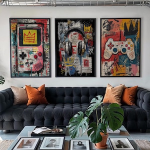 May include: Three framed abstract art pieces with gaming themes. The artwork features a handheld game console, headphones, and a game controller, all with graffiti-style backgrounds. The colour palette includes pink, red, yellow, and blue.