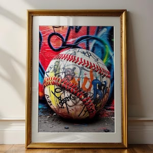 May include: A framed wall art print featuring a baseball covered in colorful graffiti and black ink markings. The baseball has prominent red stitching and is set against a vibrant, multi-colored background of spray-painted street art.