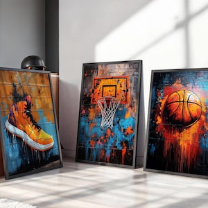 Peut inclure: Trois cadres muraux rectangulaires illustrant des thèmes de basket-ball. L'affiche de gauche montre une basket montante orange, celle du centre un panier de basket sur un mur de briques, et celle de droite un ballon de basket avec des éclaboussures.