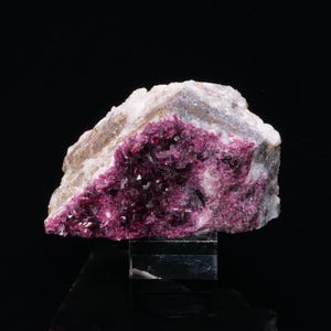 Puede incluir: Un cúmulo de cristales rosas y morados sobre una matriz blanca. Los cristales son muy reflectantes y tienen un brillo metálico. La matriz es rugosa y texturizada.