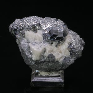 May include: A mineral specimen with a cluster of metallic, silver-grey crystals with a sparkling surface. The crystals are set against a backdrop of white, crystalline material. The specimen is mounted on a clear, rectangular base.