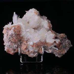 May include: A cluster of white and pink crystals on a brown rock. The crystals are arranged in a cluster and have a variety of shapes and sizes. The rock is rough and textured.