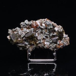 May include: A cluster of green and brown crystals on a black background. The crystals are arranged in a random pattern and are of varying sizes. The crystals are mounted on a metal stand.