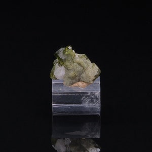 May include: A cluster of green and white crystals on a clear display stand. The crystals are arranged in a natural formation, with some of the crystals appearing to be partially embedded in the others.