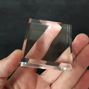 May include: A clear glass paperweight with beveled edges.