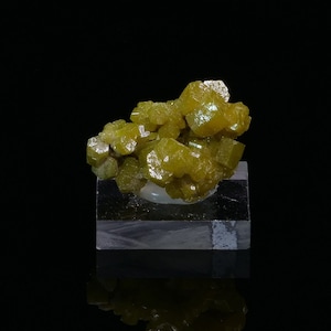 Könnte beinhalten: Ein Cluster aus leuchtend gelben, durchscheinenden Kristallen auf schwarzem Hintergrund. Die Kristalle sind in einem zufälligen, organischen Muster angeordnet und bilden ein optisch ansprechendes Display.