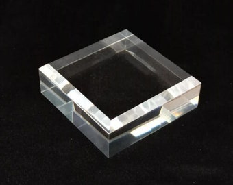 Könnte beinhalten: Ein quadratischer Acryl-Präsentationsständer aus klarem Acryl mit abgeschrägten Kanten. Der Ständer ist perfekt für die Präsentation kleiner Gegenstände wie Schmuck, Figuren oder anderer Sammlerstücke.
