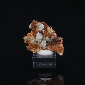 May include: A mineral specimen with light green and translucent crystals on an orange-brown rock matrix. The specimen is displayed on a clear acrylic stand against a black background.