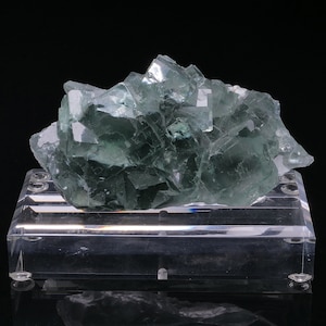 May include: A cluster of green fluorite crystals on a clear acrylic display stand. The crystals are sharp and well-defined, with a glassy lustre.