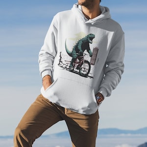 May include: A white hooded sweatshirt featuring a graphic print of a green dinosaur riding a bicycle in front of a city skyline.