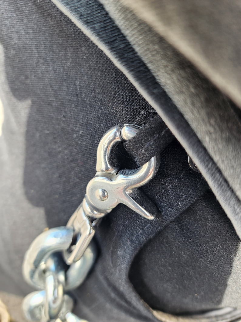 Puede incluir: Un gancho y una cadena de metal plateado unidos a una correa de tela negra.