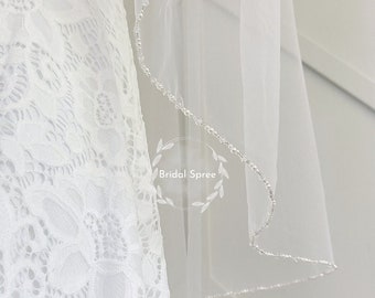 May include: A white bridal veil with a beaded edge. The veil is made of soft tulle and is perfect for a wedding.