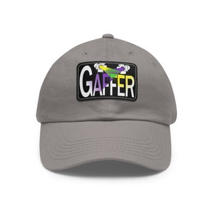 May include: A gray baseball cap with a black patch that says "GAFFER" in white letters. The patch features a stylized image of two film lights with a green, yellow, and purple design.