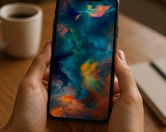 May include: A smartphone displaying a colorful abstract image of swirling blues, oranges, and greens. The phone is held in two hands, with a wooden table and a coffee cup in the background.