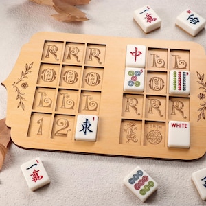May include: A wooden Mahjong game set with a light brown wooden game board and white tiles. The board has carved spaces for tiles and decorative floral accents. Several tiles are placed on the board, with others scattered around.