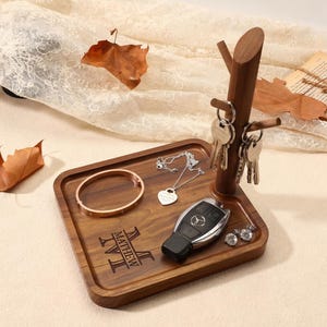 Può includere: Un vassoio in legno con portachiavi, braccialetto, collana, chiave dell'auto e orecchini. Il vassoio è inciso con il nome "MATHEW" e l'iniziale "M". Il portachiavi ha la forma di un ramo d'albero.