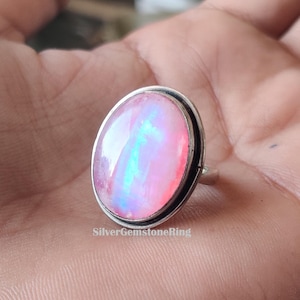 May include: A silver ring with a pink opal gemstone. The opal has a blue and green iridescent sheen.