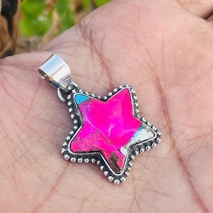 May include: A star-shaped pendant with a vibrant pink center, accented by turquoise and white sections. The pendant has a silver-colored bail and a beaded border. This jewelry item is likely a necklace pendant.