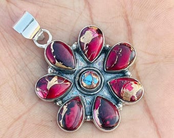 May include: A silver pendant with a flower design. The pendant features teardrop-shaped red stones with gold accents, arranged around a central turquoise stone. The pendant is held by a silver bail.