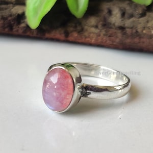 May include: A silver ring with a pink oval gemstone. The ring is set in a simple band.