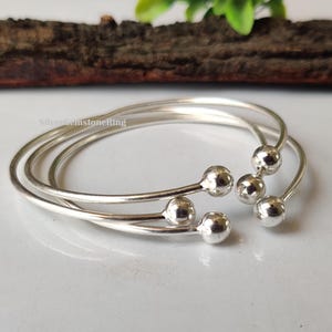 May include: Three silver bangles with small round balls at the ends. The bangles are stacked on top of each other.