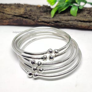May include: Set of five silver bangles with small round accents. The bangles are stacked on top of each other.