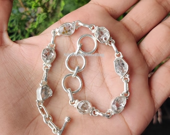 May include: A silver bracelet featuring clear, irregularly shaped gemstones. The bracelet has a toggle clasp and is composed of interconnected links. The gemstones are set in individual silver bezels, creating a delicate and elegant design.