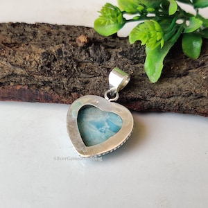 Puede incluir: Un colgante de plata en forma de coraz&oacute;n con una piedra preciosa azul y blanca engastada en el centro. El colgante tiene una anilla de plata y est&aacute; marcado con "925" en la parte posterior.
