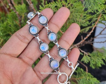 May include: A silver bracelet featuring round moonstone cabochons. The bracelet has a toggle clasp and is composed of multiple links, each with a moonstone set in a decorative bezel. The moonstones have a blue and white color.