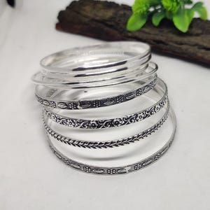 May include: Set of six silver bangles with intricate etched designs. The bangles are stacked on top of each other, showcasing the different patterns.