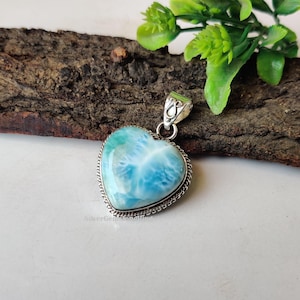 Puede incluir: Un colgante en forma de coraz&oacute;n con una piedra preciosa azul y blanca engastada en plata de ley. El colgante tiene un delicado borde de cadena de plata.
