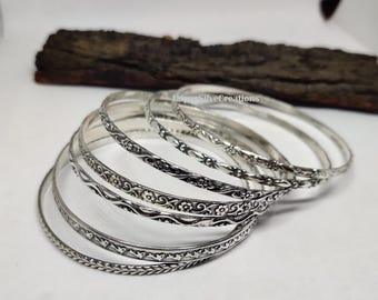 May include: Set of six silver bangles with intricate floral and geometric designs. The bangles are stacked on top of each other, showcasing the different patterns.