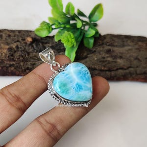Puede incluir: Un colgante de plata en forma de coraz&oacute;n con una piedra preciosa azul y verde. La piedra preciosa tiene un patr&oacute;n de remolino y est&aacute; engastada en un bisel de plata.