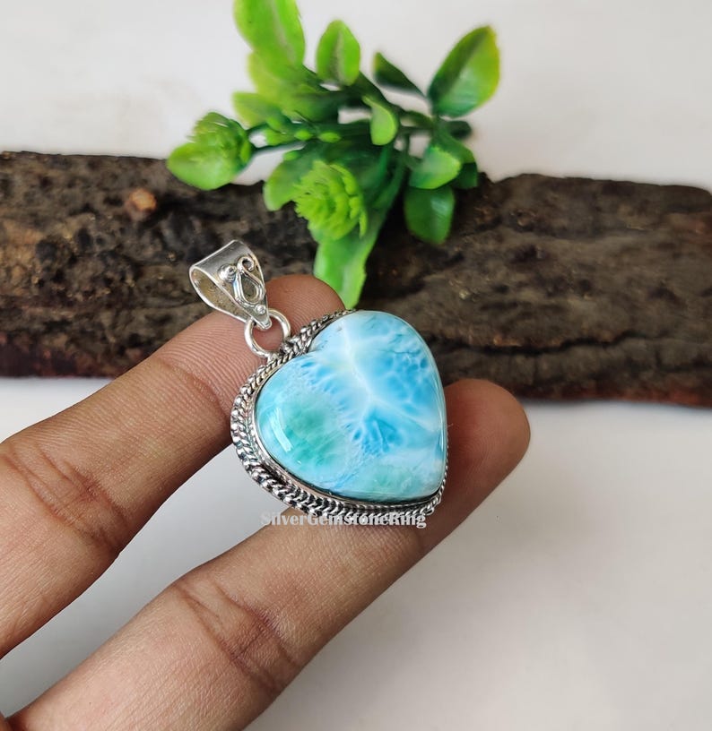 Puede incluir: Un colgante de plata en forma de coraz&oacute;n con una piedra preciosa azul y verde. La piedra preciosa tiene un patr&oacute;n de remolino y est&aacute; engastada en un bisel de plata.