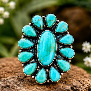 Puede incluir: Un anillo de plata con una gran piedra turquesa ovalada central rodeada por doce piedras turquesas m&aacute;s peque&ntilde;as en forma de l&aacute;grima. El engaste de metal tiene un acabado oscuro y oxidado entre las piedras, creando un dise&ntilde;o floral de alto contraste.