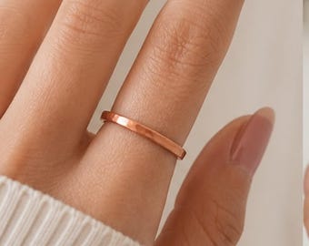 May include: A simple, smooth, polished copper-toned metal band ring with a flat profile and a consistent width, worn on a finger. The ring features a warm, metallic finish that reflects light evenly across its surface, showcasing a clean design.