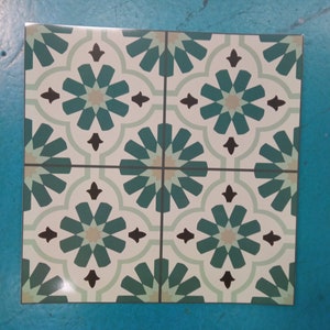 Peut inclure: Carreau carré avec un motif floral répété en vert d'eau, marron et beige sur fond blanc. Le carreau est divisé en quatre sections, chacune présentant une partie du motif. Le carreau est posé sur une surface bleue.
