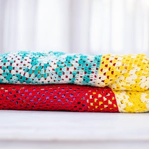 Può includere: Un mucchio di coperte all'uncinetto colorate in giallo, bianco, turchese e rosso.