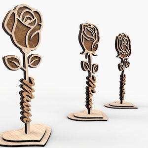 May include: Three wooden rose decorations with a heart-shaped base. The roses are cut out and have a brown wood finish. The stems are wrapped with the word "Mom" in a cursive font.