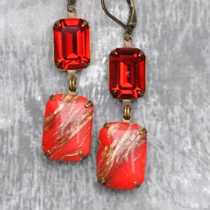 Könnte beinhalten: Ein Paar Hängeohrringe mit roten und goldenen Glassteinen. Die Ohrringe haben einen Hakenverschluss.