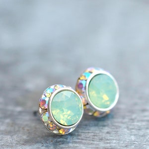 May include: A pair of silver stud earrings with a light green opal stone surrounded by iridescent crystals.