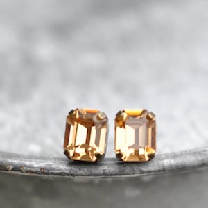 Può includere: Un paio di orecchini dorati con pietre quadrate di colore ambrato.