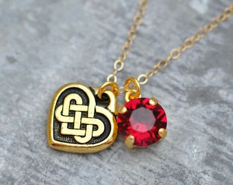 May include: A gold chain necklace with a heart-shaped pendant featuring a Celtic knot design and a red rhinestone charm.