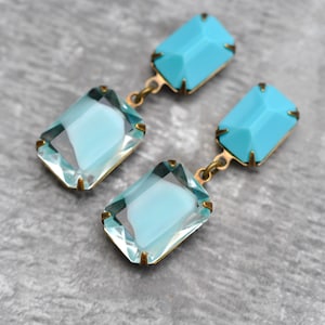 Könnte beinhalten: Ein Paar Hängeohrringe mit zwei rechteckigen türkisblauen Steinen an jedem Ohrring. Die Steine sind in goldfarbenem Metall gefasst.